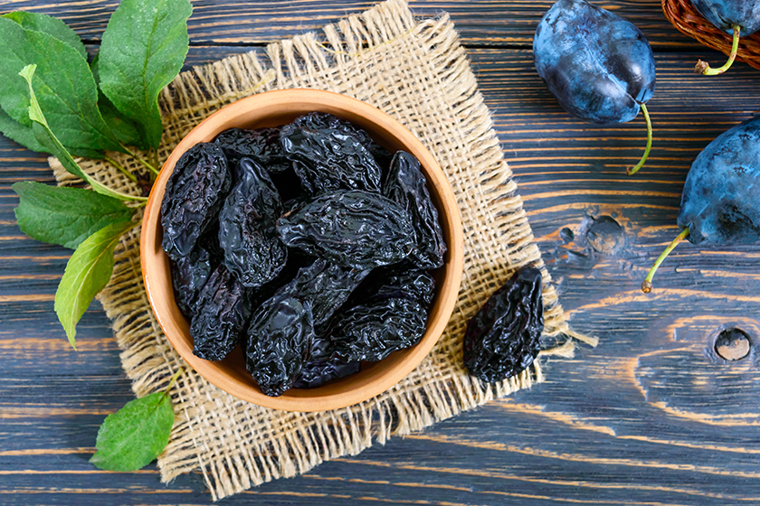 Prunes in a clay bowl and fresh plums, leaves on a wooden table. Fresh prunes for healthy life. 